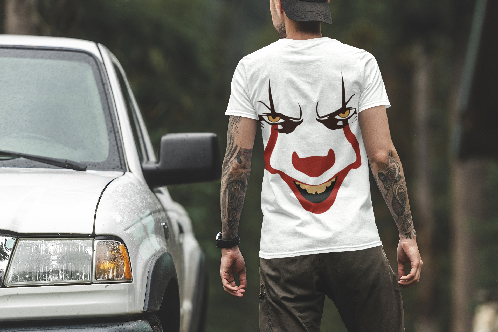 Person wearing a white t-shirt with Pennywise clown face design, standing next to a car.