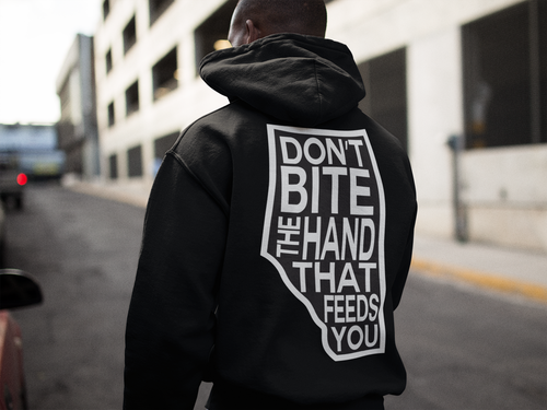 Person wearing a black hoodie with a motivational quote on the back, standing on an urban street.